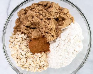 Top down view of crunch topping ingredients in a bowl including flour, oats, cinnamon, and brown sugar. Hostess At Heart