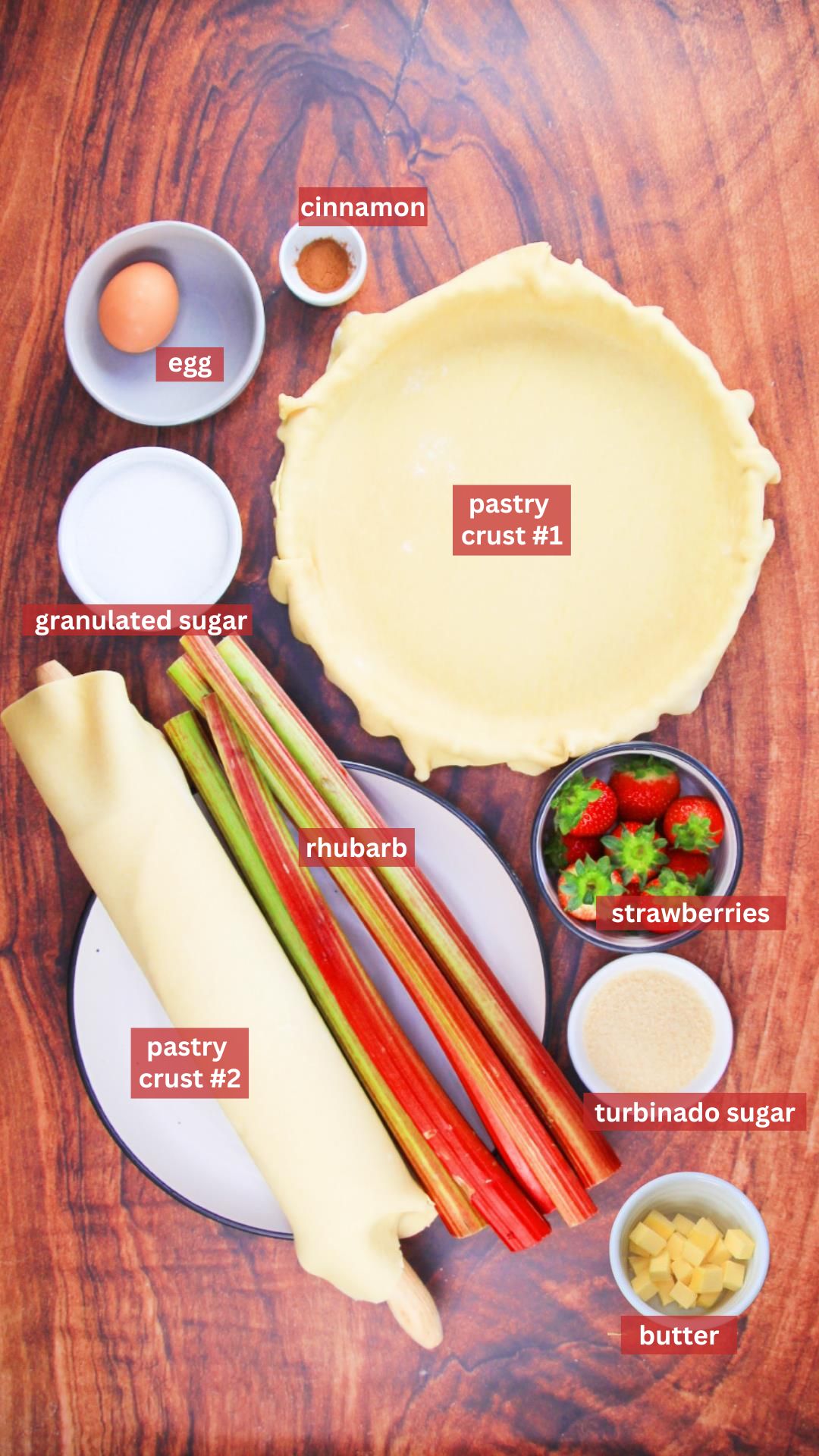 Top down view of rhubarb strawberry pie ingredients including rhubarb, strawberries, pastry crust, sugar, butter, cinnamon and an egg. Hostess At Heart