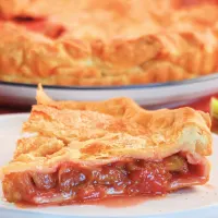 Side view of a slice of juicy strawberry rhubarb pie sitting on a plate - Hostess At Heart