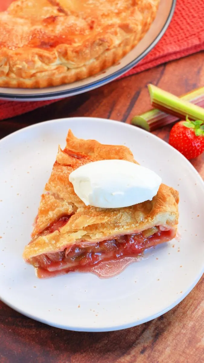 Angled view of a slice of rhubarb and strawberry pie with a dollop of ice cream