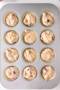 Top down view of a muffin tin lined with paper liners and filled with cherry muffin batter - Hostess At Heart