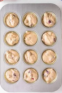 Top down view of a muffin tin lined with paper liners and filled with cherry muffin batter - Hostess At Heart