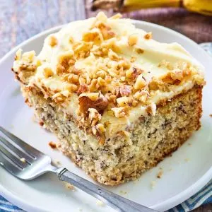 Angled view of a single piece of banana cake frosted with cream cheese frosting and garnished with chopped walnuts - Hostess At Heart