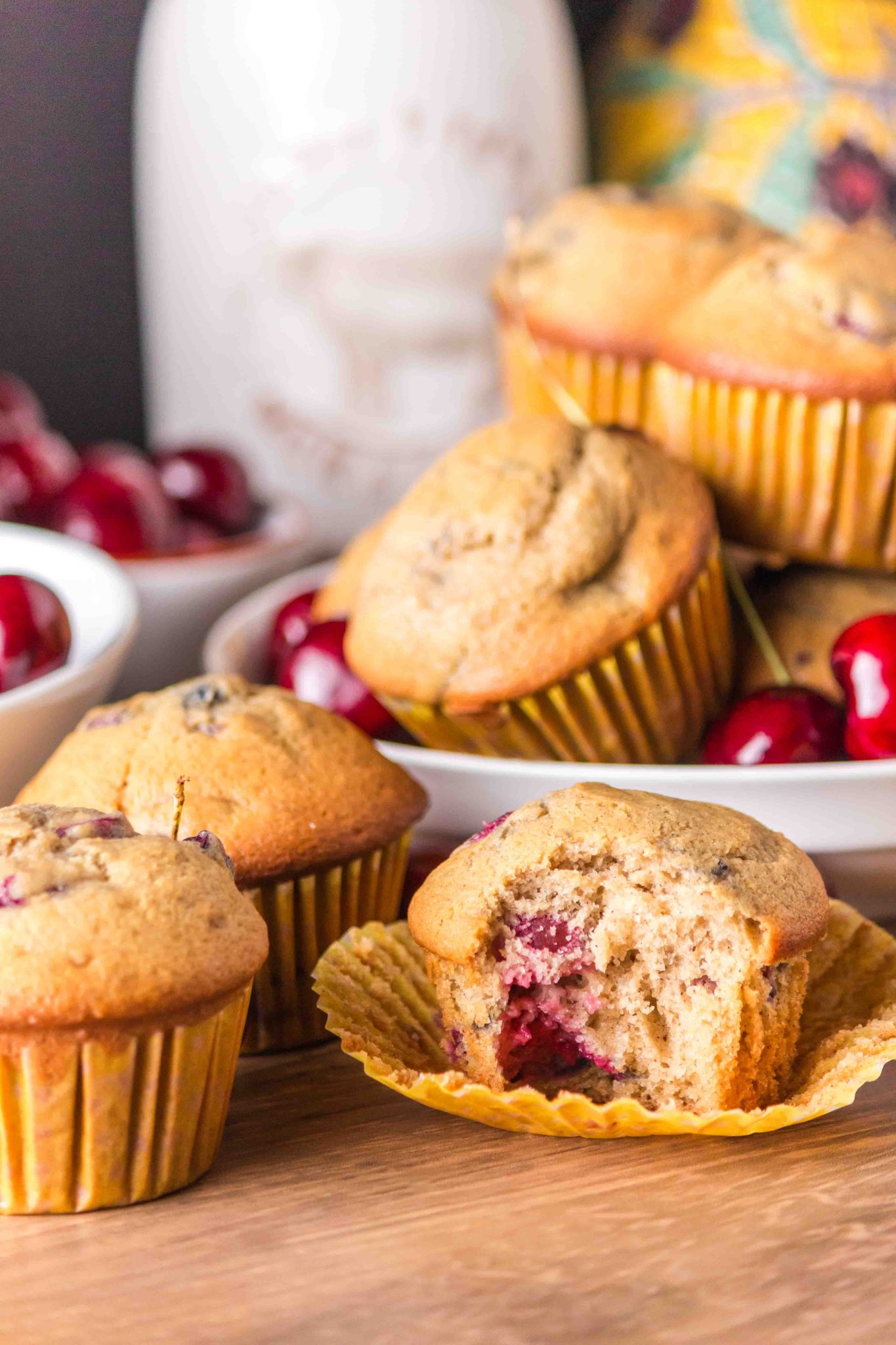 Sideview of baked cherry muffins with the front one bitten in showing the soft crumb and cherries. Hostess At Heart