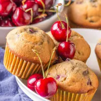 A bowl filled with baked cherry muffins surrounded by fresh cherries - Hostess At Heart