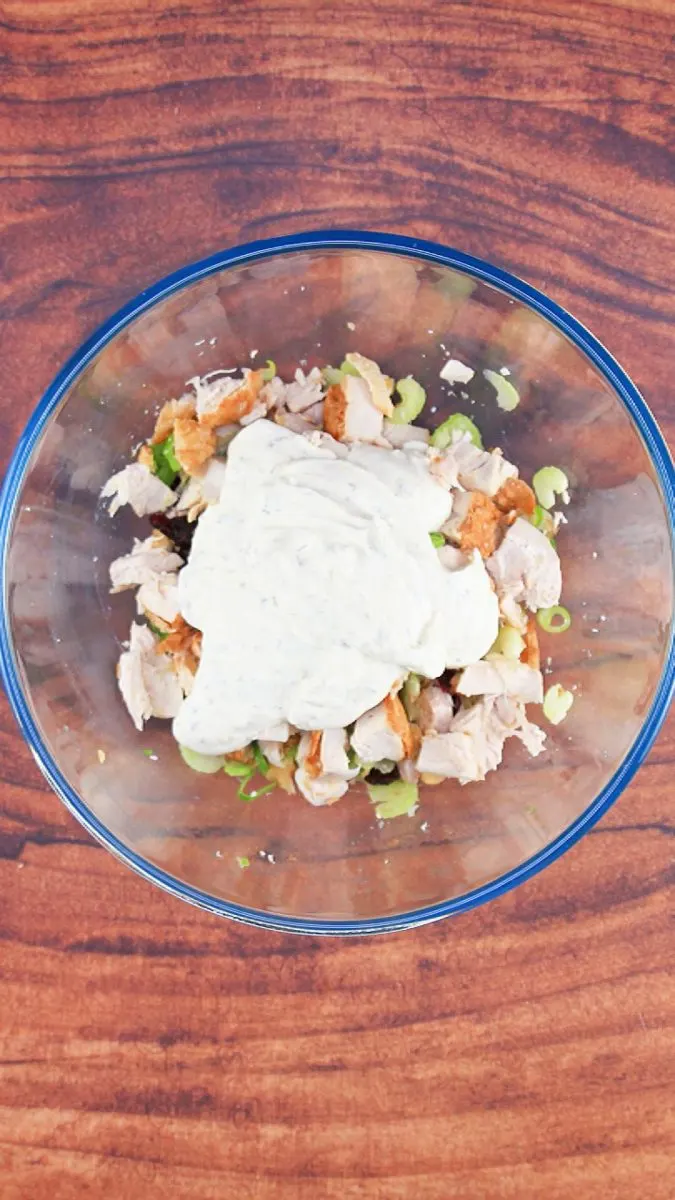 Top down view of a bowl filled with chicken salad ingredients topped with a yoghurt sauce. Hostess At Heart