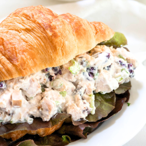 A croissant roll sliced in half and filled with creamy chicken salad on a plate - Hostess At Heart