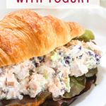 A sideview of a split croissant roll filled with healthy chicken salad on a plate - Hostess At Heart