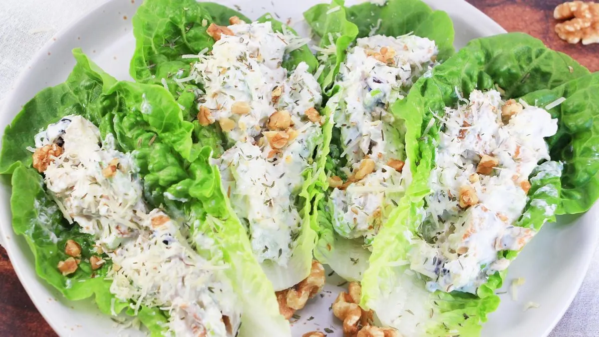 Angled view of 4 romaine lettuce leaves topped with chicken salad made with yogurt, garnished with parmesan and chopped walnuts. Hostess At Heart