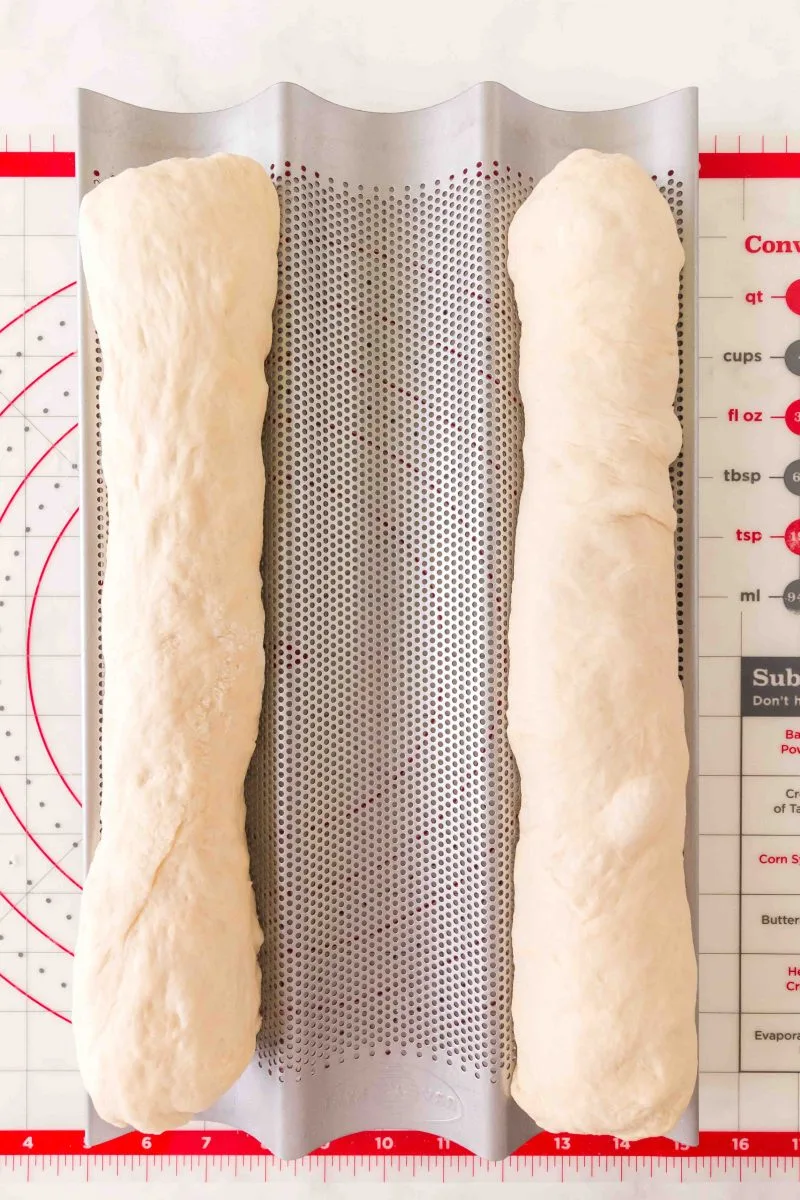 Two shaped loaves of French Bread dough sitting on a French baking pan.