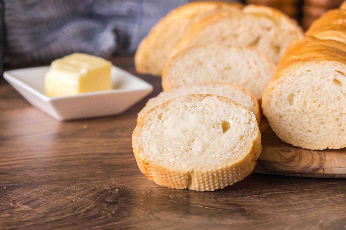 A cutting board with sliced french bread gathered around an uncut loaf. Hostess At Heart