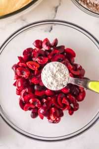 A bowl of fresh cherries with a teaspoon of flour hovering over the top.