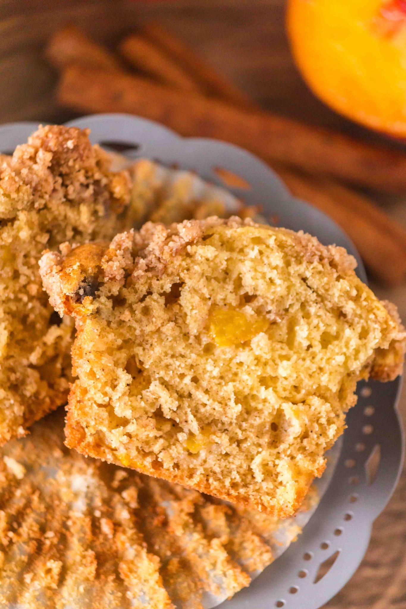 Top Down view of a baked peach muffin cut in half showing pieces of fresh peaches in a soft muffin crumb. Hostess At Heart
