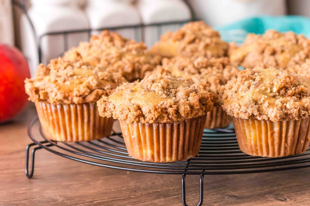 A sideview of baked peach muffins with crumble topping sitting on a cooling rack - Hostess At Heart
