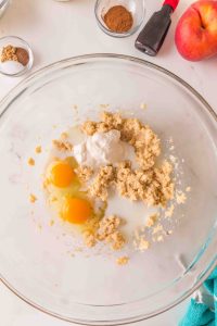 A mixing bowl with fluffy butter with sugar topped with two raw eggs and yogurt - Hostess At Heart