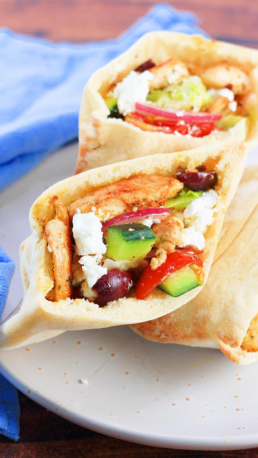 An angled top down view of a soft pita filled with browned chicken, cucumbers, lettuce and olives - Hostess At Heart