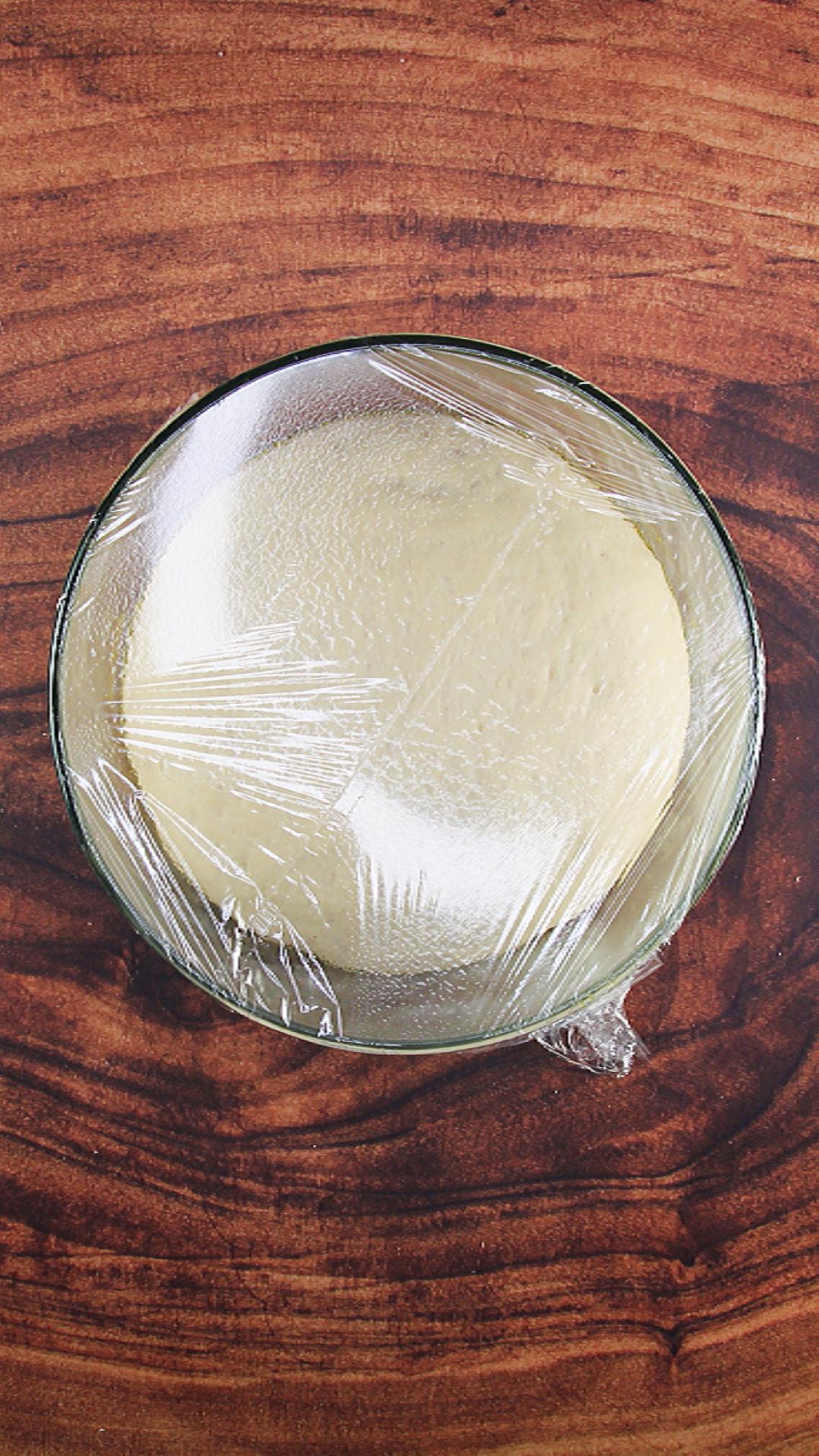 Top down view of smooth pita dough rising in a bowl.