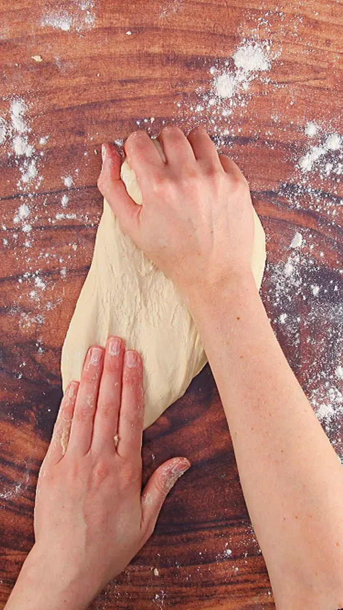 Two hands kneading dough smooth.