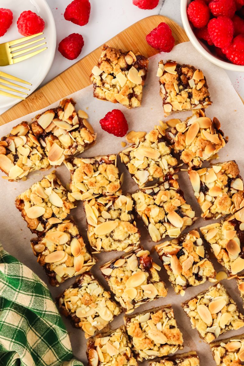 Top down view of raspberry squares topped with almond and crumbl on a pies of parchment paper - Hostess at Heart