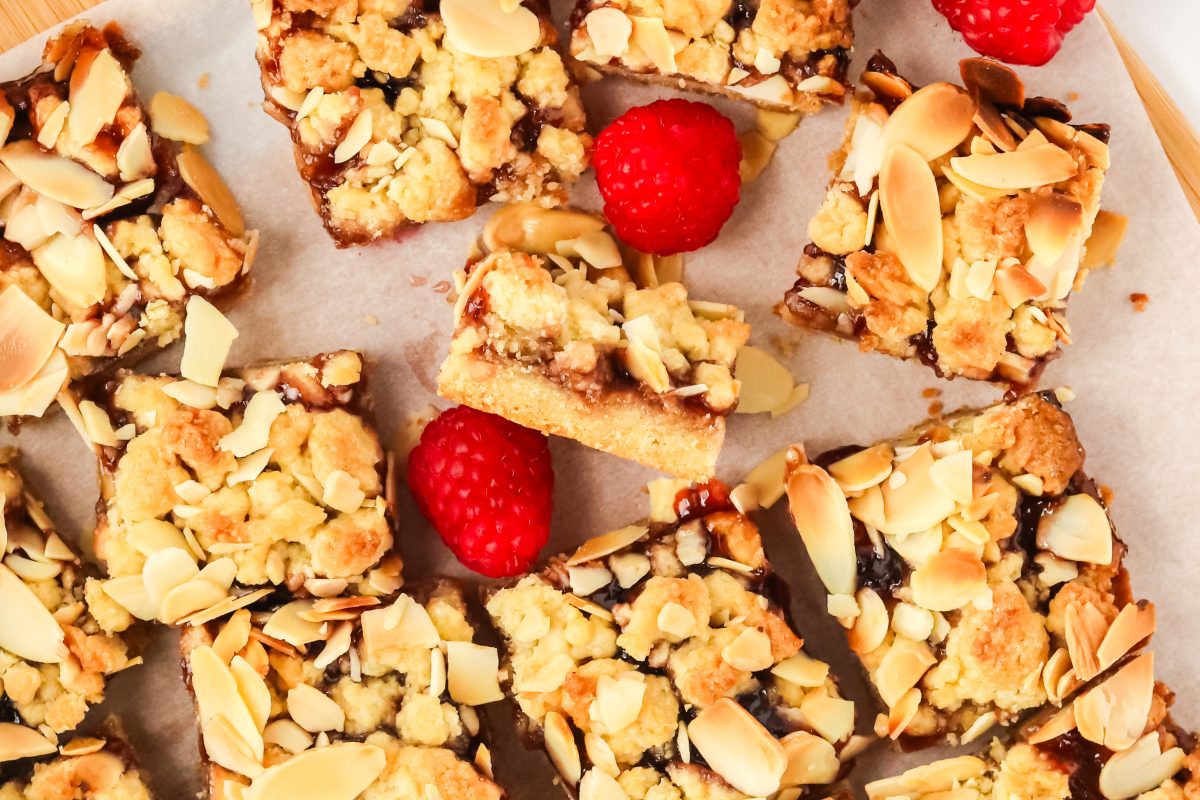 Slices of jam bars topped with almond crumble sitting on a piece of parchment paper.