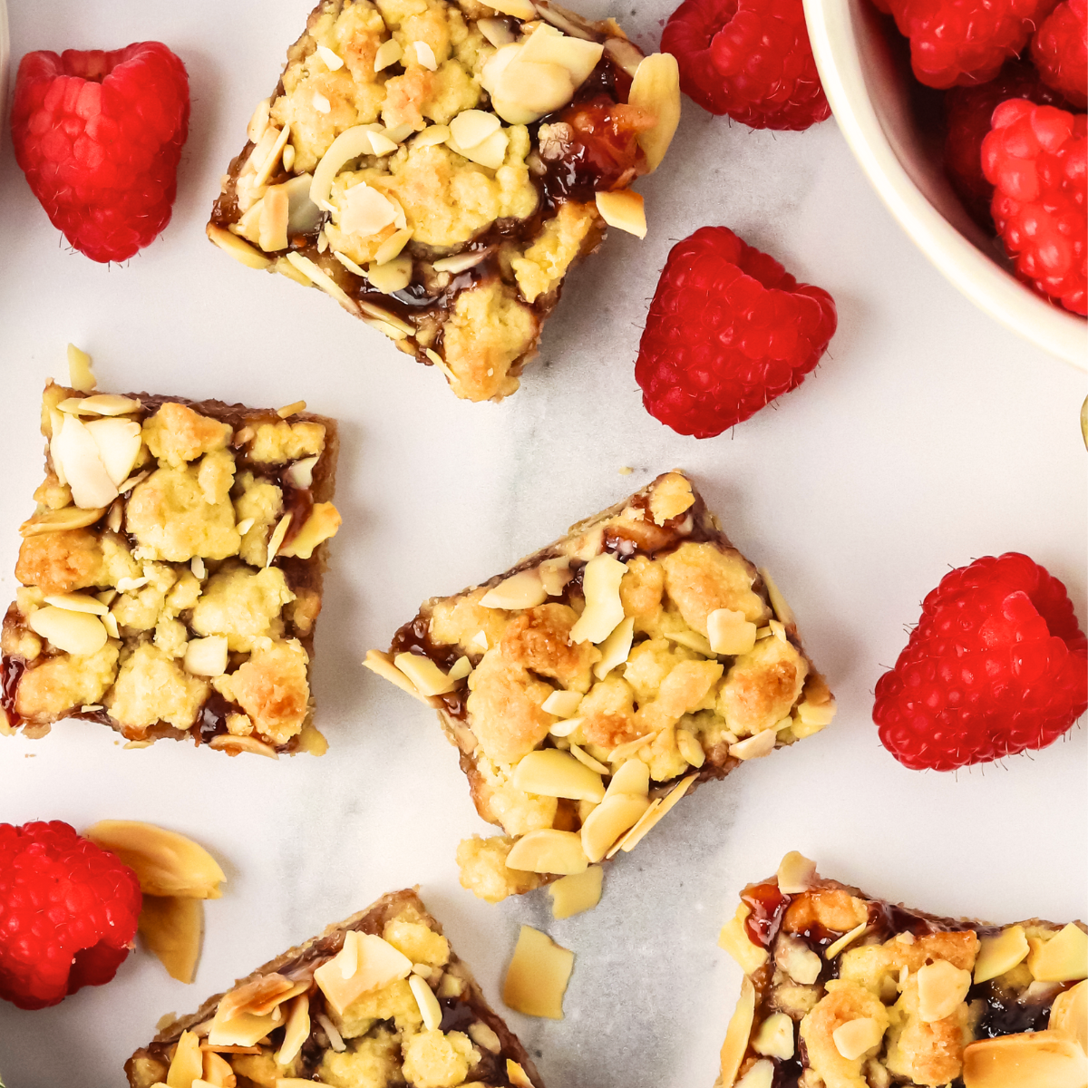 Top down view of sliced dessert bars oozing with raspberry jelly and topped with almond crumble. Hostess At Heart