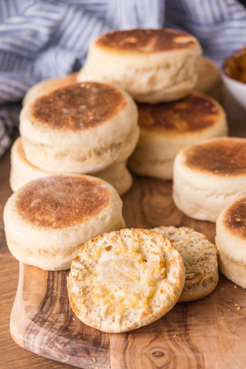 A wooden cutting board filled with baked English Muffins with a split one dripping with melted butter - Hostess At Heart