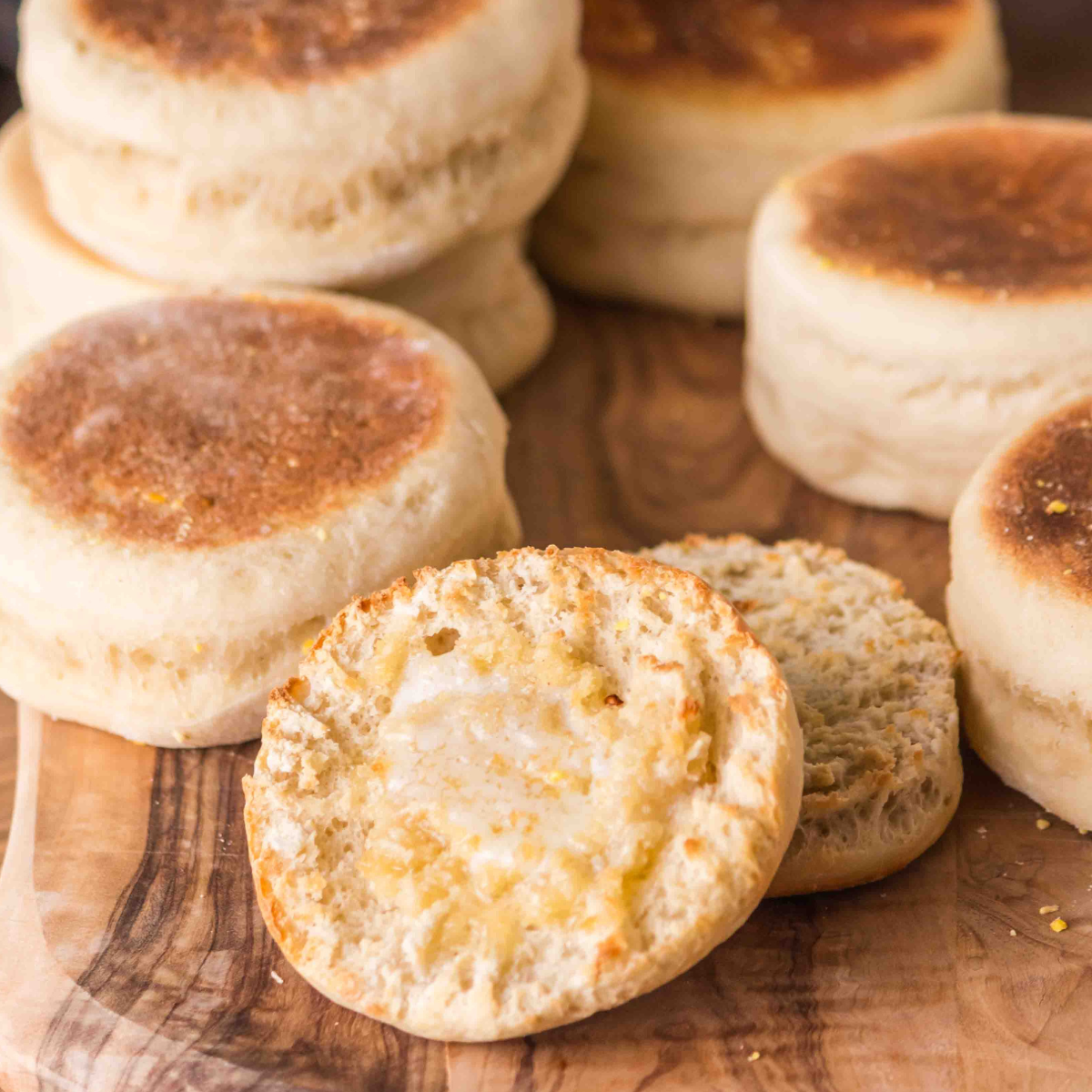 A cutting board filled with baked sour dough english muffins with a split one dripping with melted butter - Hostess At Heart