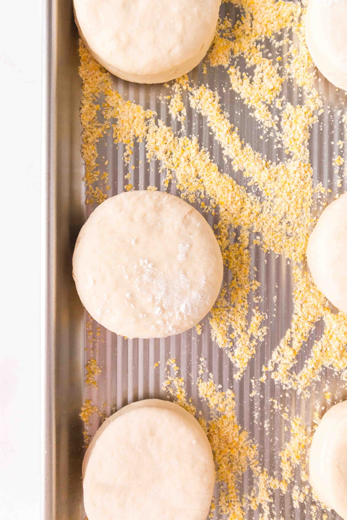 Top down view of cut English Muffins sitting on a baking sheet dusted with cornmeal - Hostess At Heart