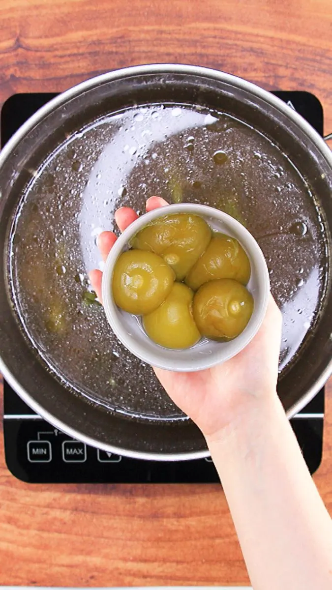 A bowl filled with 5 tomatillos hovering over a cooking pot - Hostess At Heart