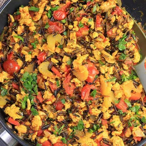 A skillet filled with Turmeric Chicken with wild rice, red pepper, onion, celery and garnished with parsley - Hostess At Heart