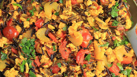 A skillet filled with Turmeric Chicken with wild rice, red pepper, onion, celery and garnished with parsley - Hostess At Heart