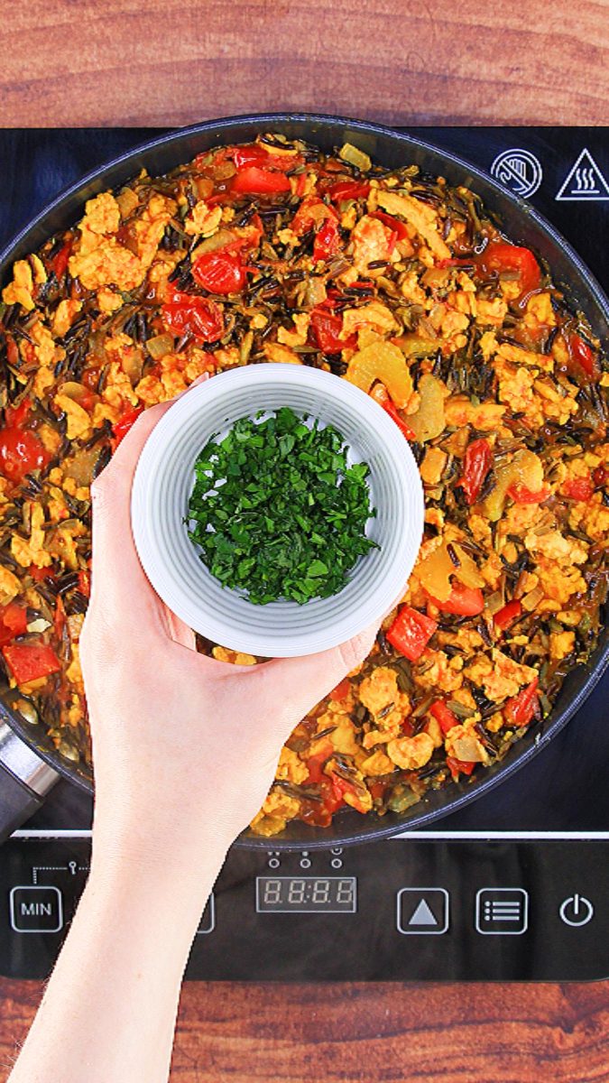 A small bowl filled with freshly chopped parsley hovering over a skillet filled with cooked chicken and wild rice - hostess at heart