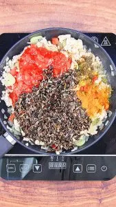 A skillet with cooked wild rice, diced tomatoes, and turmeric over cooked chicken mix - Hostess At Heart