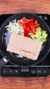 Skillet filled with ground chicken, celery, red peppers, and onion.