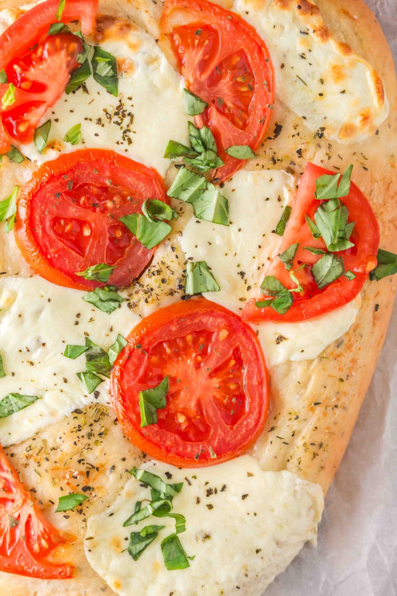 Top down view of a baked flatbread pizza topped with fresh tomatoes, melted mozzarella, and fresh sweet basil - Hostess At Heart