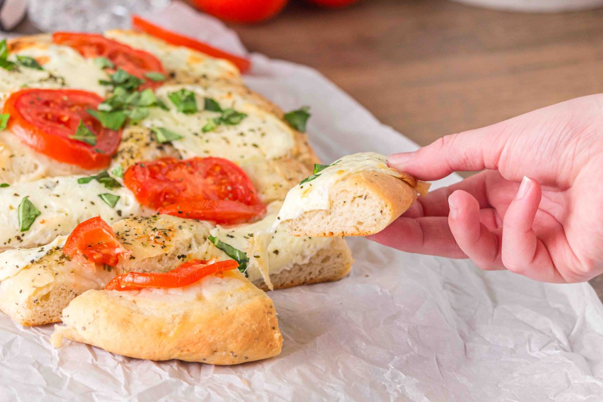 An image for Pinterest of a Margherita flat bread pizza that's been sliced and a hand pulling a slice away from the whole pizza. Hostess At Heart