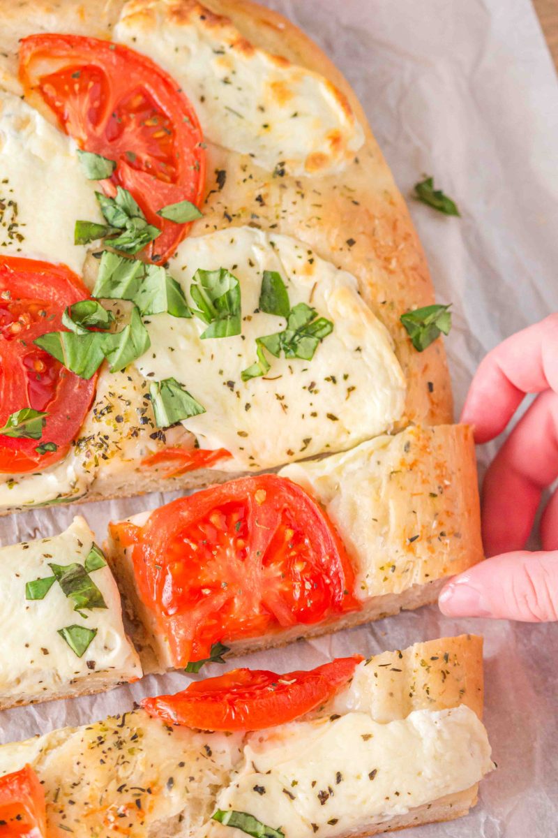 Top down view of a sliced flatbread pizza topped with fresh tomatoes, fresh mozzarella, and herbs. Hostess At Heart