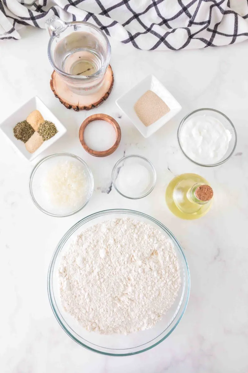 Ingredients for flatbread pizza including water, sugar, yeast, olive oil, sour cream, flour, salt, garlic powder, onion powder, Italian seasoning, basil, and Parmigiano.