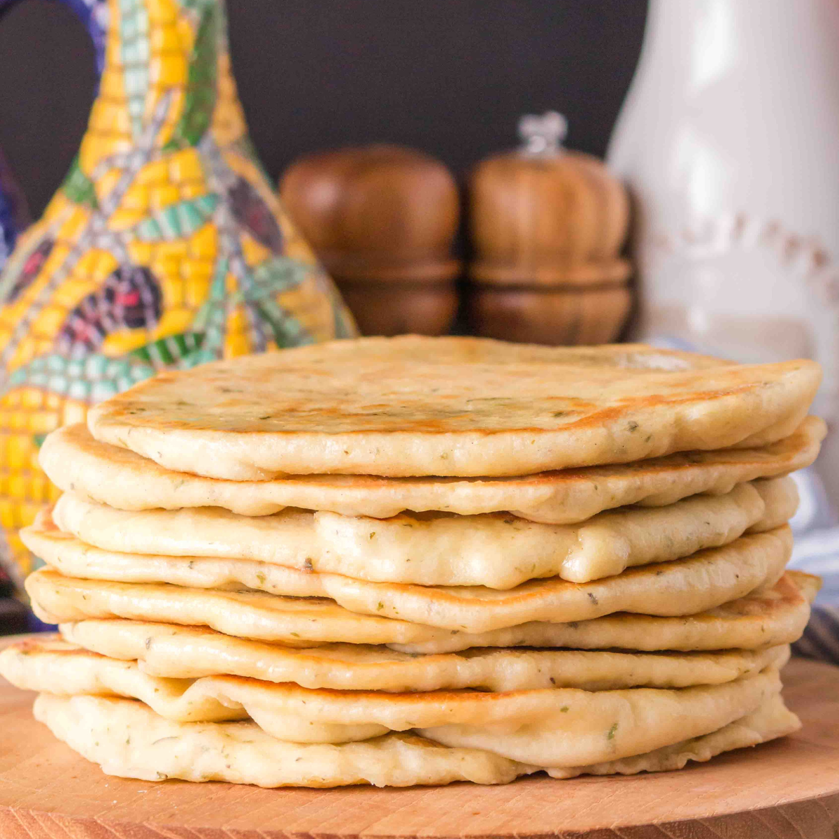 Sideview of a stack of homemade flatbread sitting on a cutting board with an olive oil caraffe in the back. HostessAtHeart.com