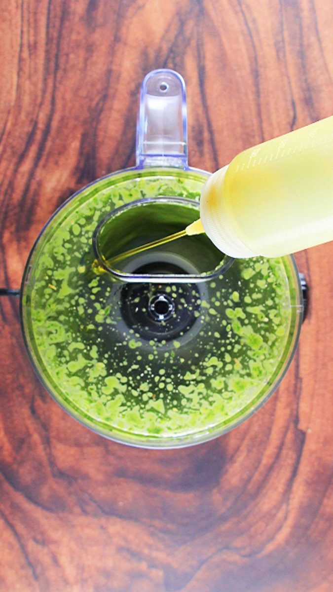 A bottle of olive oil added to a food processor filled with sweet basil to make pesto. Hostess At Heart