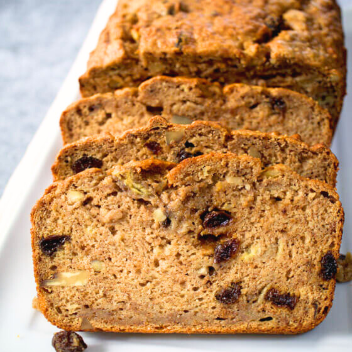 A front view of a loaf of apple banana bread with the front 3 slices leaning up against the loaf. Hostess At Heart