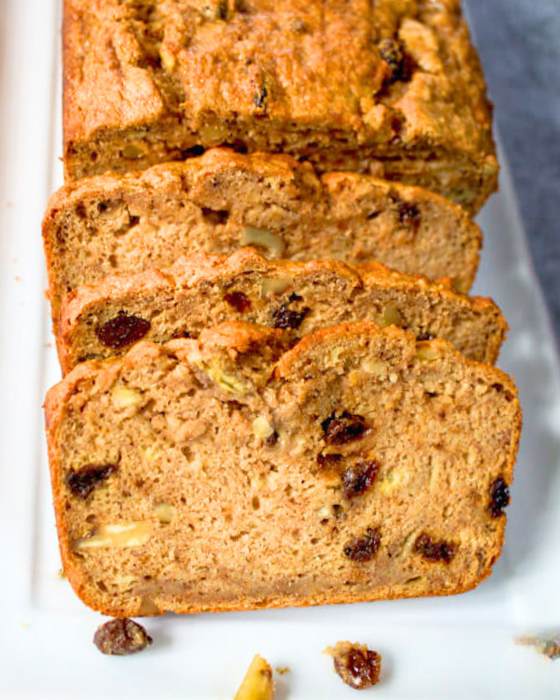 Front view of baked quick banana bread with the front slices fanned out in the front showing raisins and chopped nuts in the bread - Hostess At Heart.