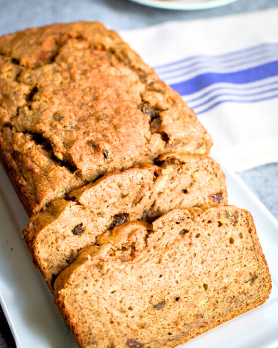 Top down view of baked banana bread sitting on a plate with the front two slices cut and fanned out in front. Hostess At Heart