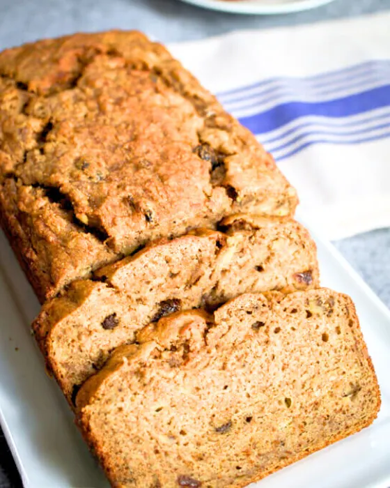 Top down view of baked banana bread sitting on a plate with the front two slices cut and fanned out in front. Hostess At Heart