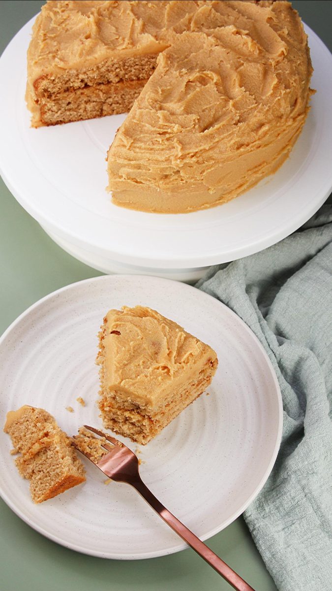 Top-down image of homemade spice cake with peanut butter frosting, on a white platter, with a slice removed and on a white pate nearby.