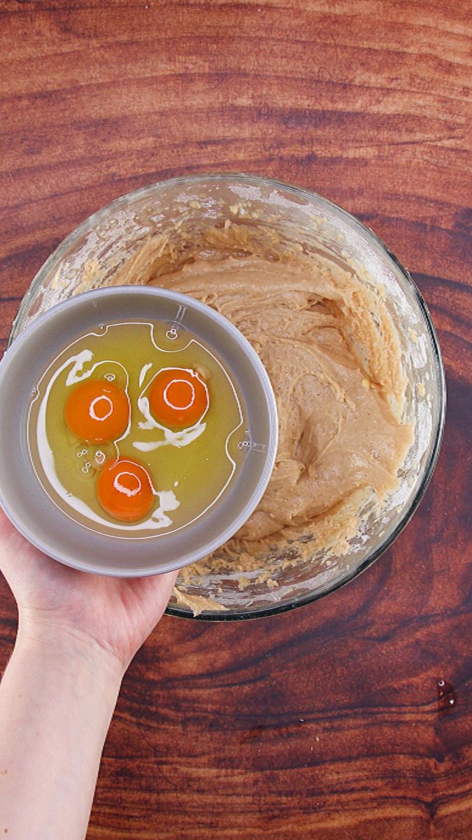 Three eggs being added to cake batter in a mixing bowl.