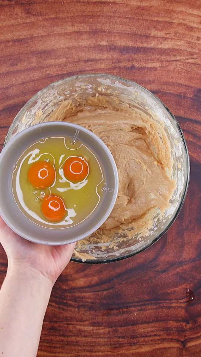 Three eggs being added to cake batter in a mixing bowl.