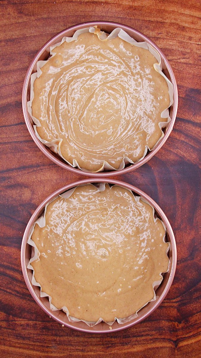 Top-down image showing the spice cake batter in two round pans lined with parchment paper.