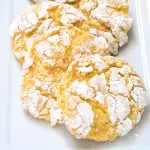 Front table view of yellow Lemon Cake Mix Cookies layered in a row on a white plate. Hostess At Heart