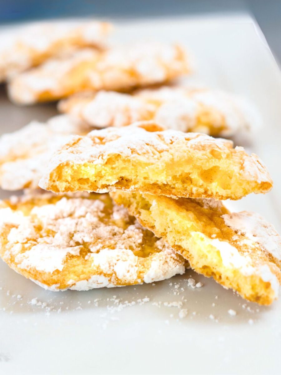 Yellow Lemon Snowflake cookies layered on a white plate with a broken cookie in the front showing the soft center.